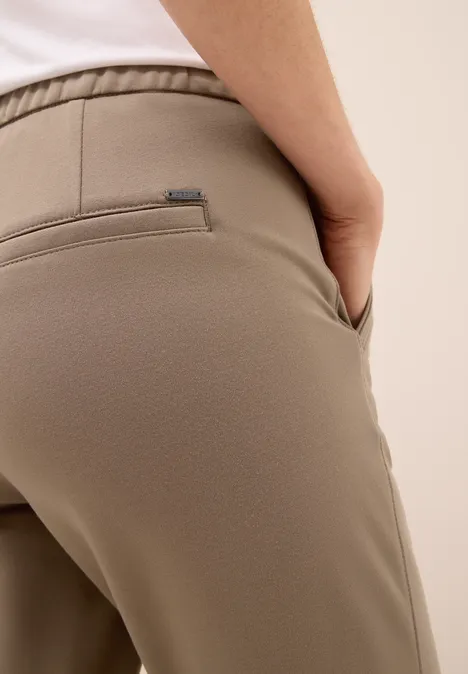 Nahaufnahme einer Person in beigefarbener Hose, Hand in der Tasche.